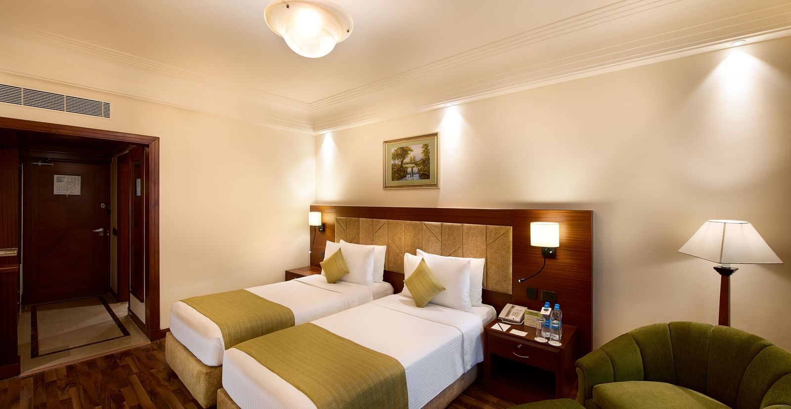 An image of a bedroom featuring twin bed, a sofa chairs, and a bedside table with lamp - Accord Hotels and Resorts